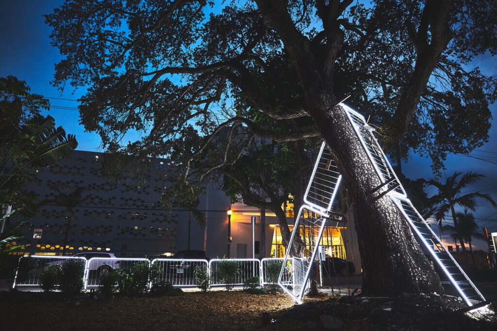 Antonia Wright and Ruben Millares mighty oaks from tiny acorns grow, 2023 Oak tree, 12 police barricades, LED lights 42’ x 14’ x 15’ approx. Installation image from Making Miami in the Design District